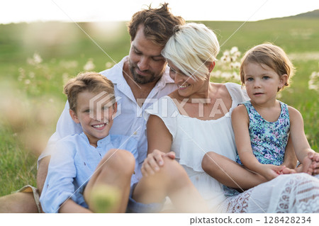 Young family enjoying peaceful summer evening outdoors in green summer nature 128428234