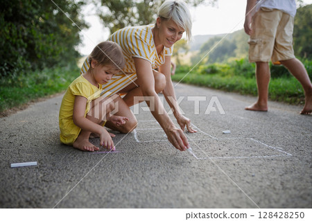 Mom and girl drawing with chalk on road. . Mom and girl drawing with chalk on road. . 128428250