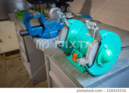 Bench grinder sitting on workbench next to vise in workshop Bench grinder sitting on workbench next to vise in workshop 128428338