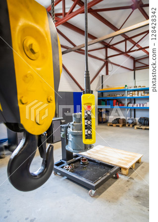 Yellow overhead crane remote control hanging in factory 128428342