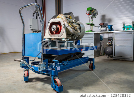 Hydraulic scissor lift cart holding industrial pump in workshop 128428352