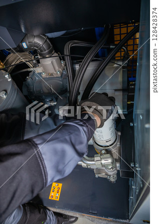 Technician replacing oil filter in industrial compressor, maintenance procedure Technician replacing oil filter in industrial compressor, maintenance procedure 128428374