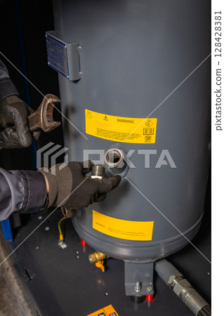 Technician repairing industrial compressor with wrench and replacement part 128428381