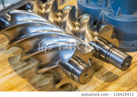 Shiny new screw compressor rotor resting on wooden table 128428413