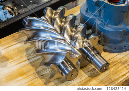 Shiny new screw compressor rotor resting on wooden workbench Shiny new screw compressor rotor resting on wooden workbench 128428414