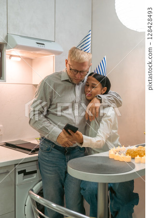 Here's a title following your specifications: Birthday Selfie Kitchen Father Daughter: Happy grandfather and granddaughter take a celebratory selfie together in their kitchen during a birthday 128428493