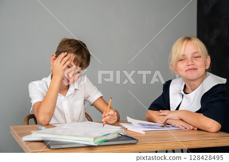 Boy Girl Homework - Boy doing homework at a table while girl looks on. 128428495