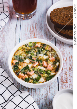 Vegetables sausage kvass soup with herbs in a bowl on the table vertical view 128428595