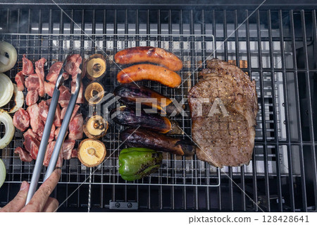 Barbecue scene with meat being grilled with tongs Barbecue scene with meat being grilled with tongs 128428641