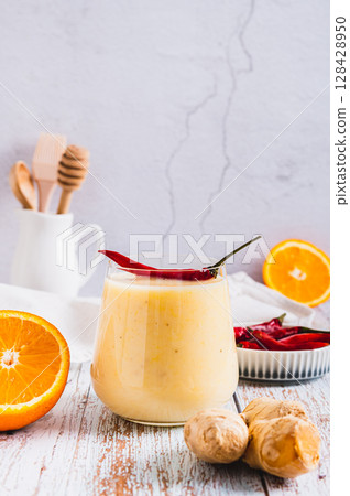 Smoothie with orange, ginger and cayenne pepper in a glass on the table vertical view Smoothie with orange, ginger and cayenne pepper in a glass on the table vertical view 128428950