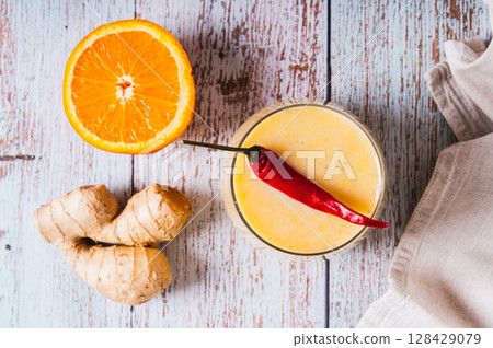 Close up of smoothie with orange, ginger and cayenne pepper in a glass on the table top view 128429079