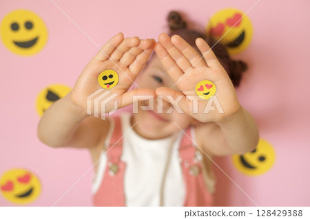 Two yellow emoticons on the palms of the child. World Emoji Day is on July 17th. Smile face Day Two yellow emoticons on the palms of the child. World Emoji Day is on July 17th. Smile face Day 128429388