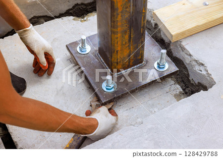 Contractor worker attaches steel column to concrete base with bolts during works daytime project. Contractor worker attaches steel column to concrete base with bolts during works daytime project. 128429788