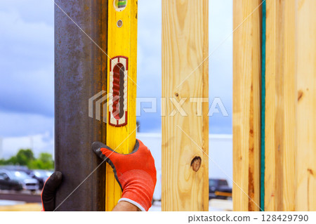 Worker checks vertical alignment of wooden beams using spirit level at construction site during work time 128429790