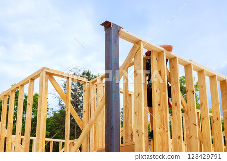 Construction worker erects wooden framing for building under works day surrounded by greenery. 128429791