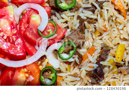 A close-up of pilaf garnished with a salad of chopped tomatoes, onions, and green chili peppers. This photo can be used in any food-themed design 128430198