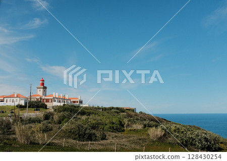 Scenic landscape of Cabo da Roca lighthouse with blue sky dramatic cliffs Atlantic Ocean rugged coastline in Sintra Portugal popular travel destination viewpoint with natural vegetation. High quality 128430254