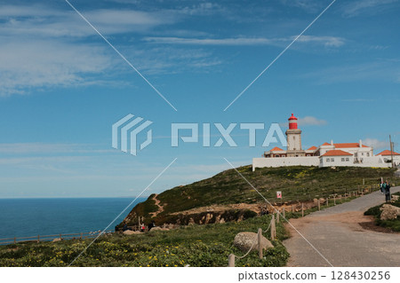 Lush green hills and rugged terrain with blue sky and scattered clouds in Cabo da Roca Sintra Portugal natural landscape with vegetation from scenic hiking trail 128430256