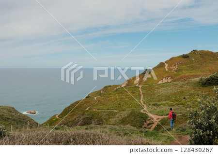Hikers walking along scenic coastal trail at Cabo da Roca Sintra Portugal with grassy cliffs overlooking Atlantic Ocean under cloudy sky westernmost mainland Europe outdoor travel landscape. High Hikers walking along scenic coastal trail at Cabo da Roca Sintra Portugal with grassy cliffs overlooking Atlantic Ocean under cloudy sky westernmost mainland Europe outdoor travel landscape. High 128430267