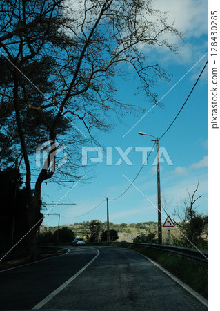 Scenic coastal road with view of Cabo da Roca lighthouse in Sintra Portugal curving highway through natural cliffs overlooking Atlantic Ocean under clear blue sky 128430285