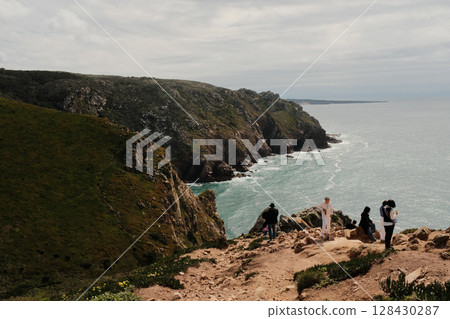 Lush green hills and rugged terrain with blue sky and scattered clouds in Cabo da Roca Sintra Portugal natural landscape with vegetation from scenic hiking trail 128430287