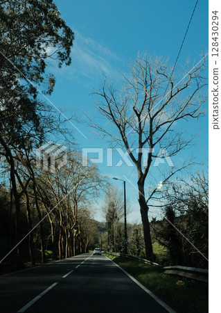 Scenic coastal road with view of Cabo da Roca lighthouse in Sintra Portugal curving highway through natural cliffs overlooking Atlantic Ocean under clear blue sky 128430294