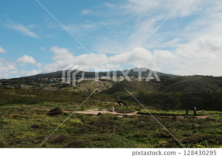 Lush green hills and rugged terrain with blue sky and scattered clouds in Cabo da Roca Sintra Portugal natural landscape with vegetation from scenic hiking trail. High quality photo Lush green hills and rugged terrain with blue sky and scattered clouds in Cabo da Roca Sintra Portugal natural landscape with vegetation from scenic hiking trail. High quality photo 128430295