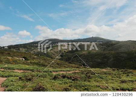 Lush green hills and rugged terrain with blue sky and scattered clouds in Cabo da Roca Sintra Portugal natural landscape with vegetation from scenic hiking trail. High quality photo Lush green hills and rugged terrain with blue sky and scattered clouds in Cabo da Roca Sintra Portugal natural landscape with vegetation from scenic hiking trail. High quality photo 128430296