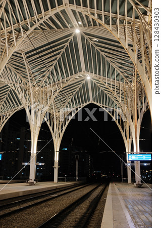 Modern illuminated architecture of Oriente Station at night in Lisbon Portugal featuring geometric roof design arches and empty railway tracks in futuristic urban environment. High quality photo Modern illuminated architecture of Oriente Station at night in Lisbon Portugal featuring geometric roof design arches and empty railway tracks in futuristic urban environment. High quality photo 128430303