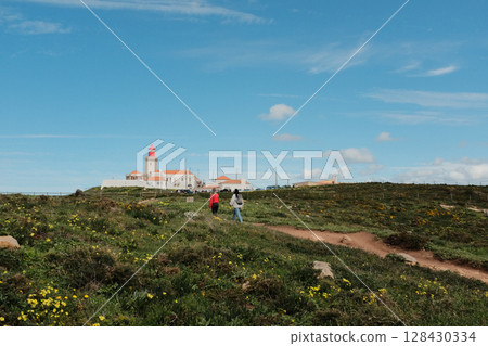 Lush green hills and rugged terrain with blue sky and scattered clouds in Cabo da Roca Sintra Portugal natural landscape with vegetation from scenic hiking trail 128430334