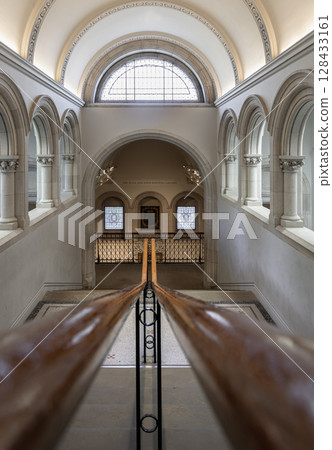 a grand staircase with a prominent wooden handrail leading towards a large arched window at the top, a grand staircase with a prominent wooden handrail leading towards a large arched window at the top, 128433161