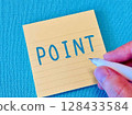 A hand writing "POINT" in blue on a sticky note 128433584