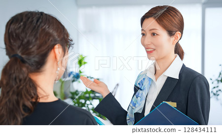 Smiling female store clerk/reception staff serving customers 128434111