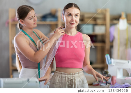 Young female seamstress adjusting clothes on adult woman Young female seamstress adjusting clothes on adult woman 128434936