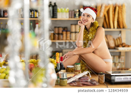 Topless girl celebrates Christmas on table near supermarket display window 128434939