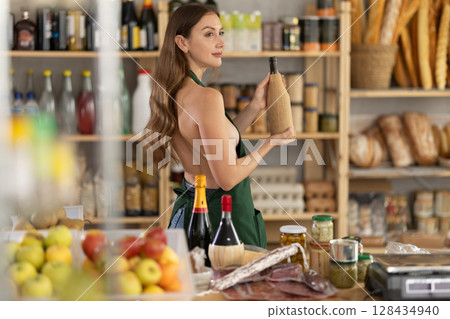 Young woman in apron with wine in grocery store Young woman in apron with wine in grocery store 128434940
