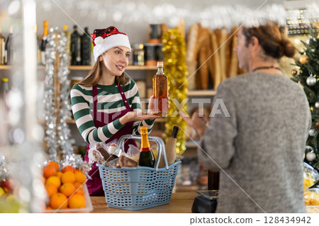 Smiling saleswoman assisting customer with Christmas spirits selection 128434942