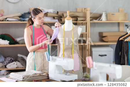 Woman seamstress adjusts clothes on mannequin Woman seamstress adjusts clothes on mannequin 128435082