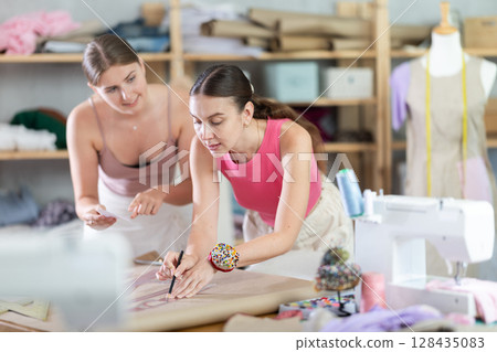 Young and adult female seamstresses drawing pattern on paper Young and adult female seamstresses drawing pattern on paper 128435083