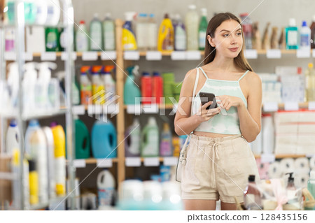 Woman scrolling through shopping list on phone while standing in supermarket 128435156