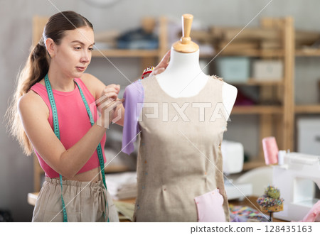 Woman seamstress adjusts clothes on mannequin Woman seamstress adjusts clothes on mannequin 128435163