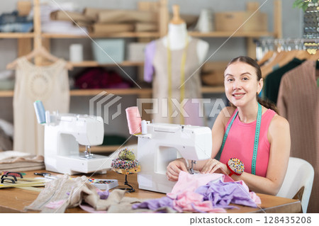 Woman seamstress sews on sewing machine in workshop Woman seamstress sews on sewing machine in workshop 128435208