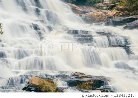 Beautiful waterfall with a lush green forest in the background. The water is flowing down the rocks and creating a beautiful scene. Sustainable waterfall in lush forest promoting water sustainability. 128435213