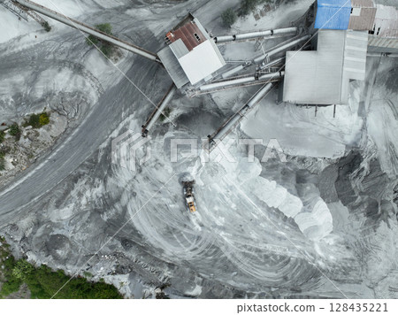 Aerial view of industrial stone crusher facility with active machinery processing raw materials in open quarry, surrounded by forest edge, highlighting environmental impact of resource extraction. 128435221