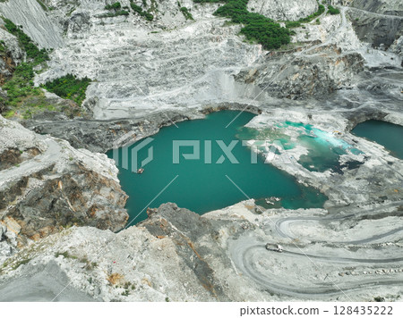 Open pit mine industry. Limestone quarry with truck. Heavy machinery in mining industry and construction material supply. Landscape of resource extraction in industrial site. Turquoise water lake. 128435222