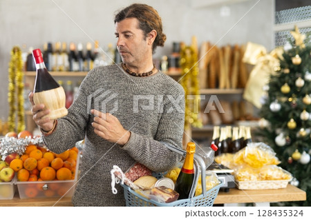 Discerning customer choosing wine for Christmas celebration in grocery store Discerning customer choosing wine for Christmas celebration in grocery store 128435324