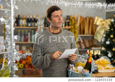 Portrait of modern man with cart shopping at supermarket, looking for something and reviewing and checking list of products to buy. Portrait of modern man with cart shopping at supermarket, looking for something and reviewing and checking list of products to buy. 128435339