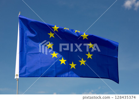 Flag of European Union flies on flagpole against blue sky 128435374
