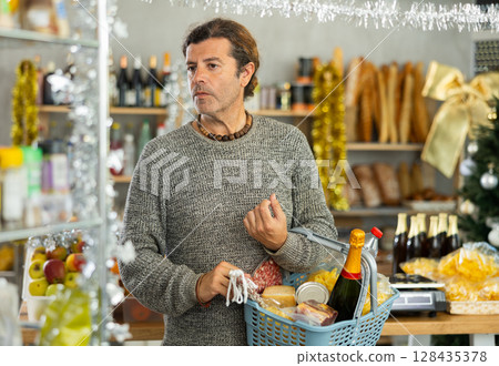 Elegant man holding shopping cart and choosing something while buying food in supermarket to Christmas table Elegant man holding shopping cart and choosing something while buying food in supermarket to Christmas table 128435378