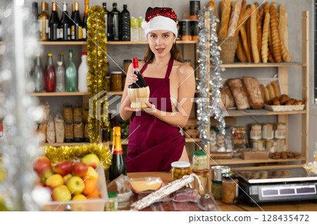 Half-naked girl in apron and Santa hat stands in store near counter Half-naked girl in apron and Santa hat stands in store near counter 128435472